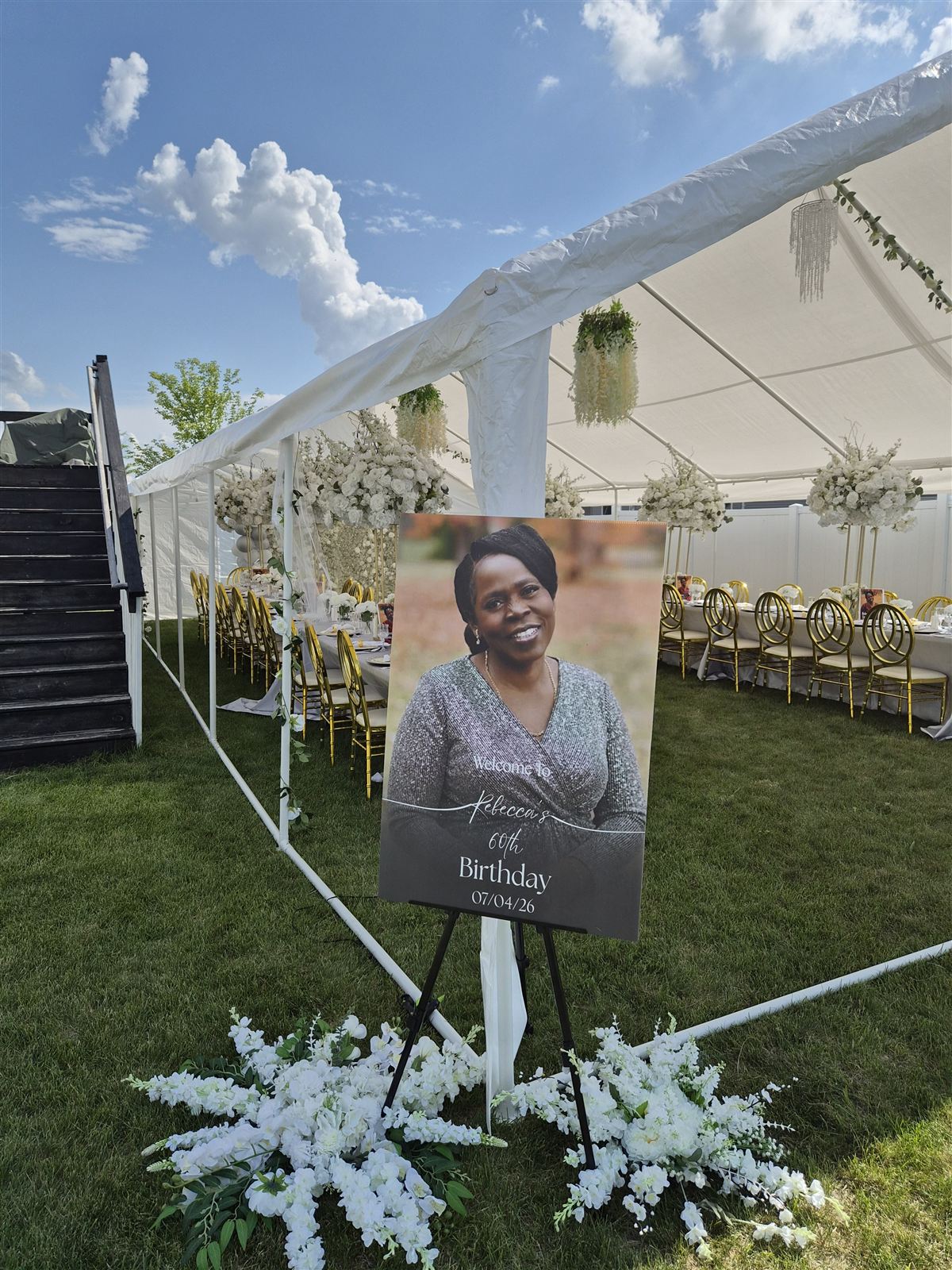 Floral-flanked welcome sign at the entrance to a tented milestone birthday reception